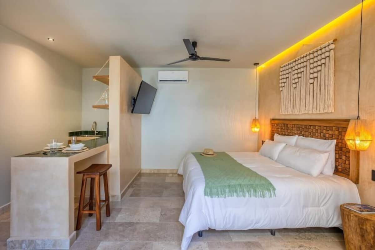Quarto com cama, escrivaninha, cadeira, ventilador de teto e ar-condicionado fixado na parede.