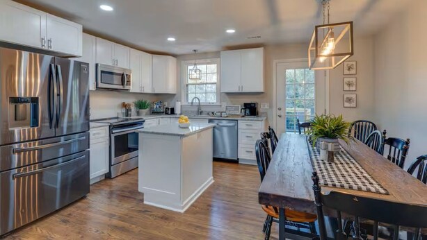 Una cocina moderna con electrodomésticos de acero inoxidable, una isla central y un comedor con mesa y sillas de madera.