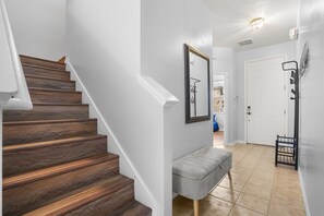 A staircase with wooden steps, a grey bench, a white door, and a wall-mounted mirror. - 3BR Villa in Gated HOA Near Disney (Kissimmee)