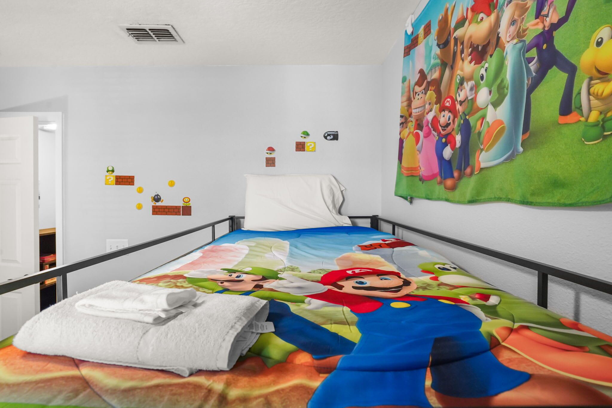 A bed with a Mario-themed bedspread, a white pillow, and a Mario poster on the wall.