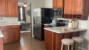A kitchen with wooden cabinets, a stainless steel refrigerator, a microwave, and a bar stool. - The Haven near the lake and Nash! 3bd/2ba (Hendersonville)