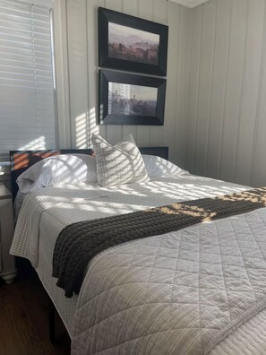 Cama bem arrumada com colcha, almofadas e manta. Duas fotos emolduradas na parede acima da cama.