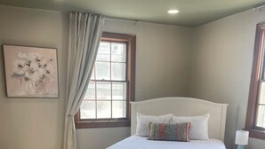A bedroom with a bed, a window with curtains, a bedside table, and a wall-mounted painting. - The Haven near the lake and Nash! 3bd/2ba (Hendersonville)