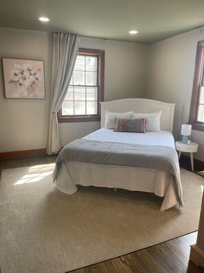Une chambre à coucher avec un lit, une fenêtre avec des rideaux, une table de chevet et un tableau accroché au mur.