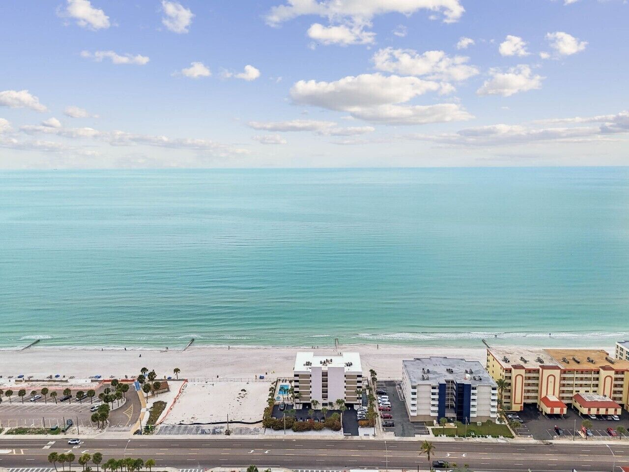 Een kusthotel met meerdere gebouwen, een strand en een weg op de voorgrond.