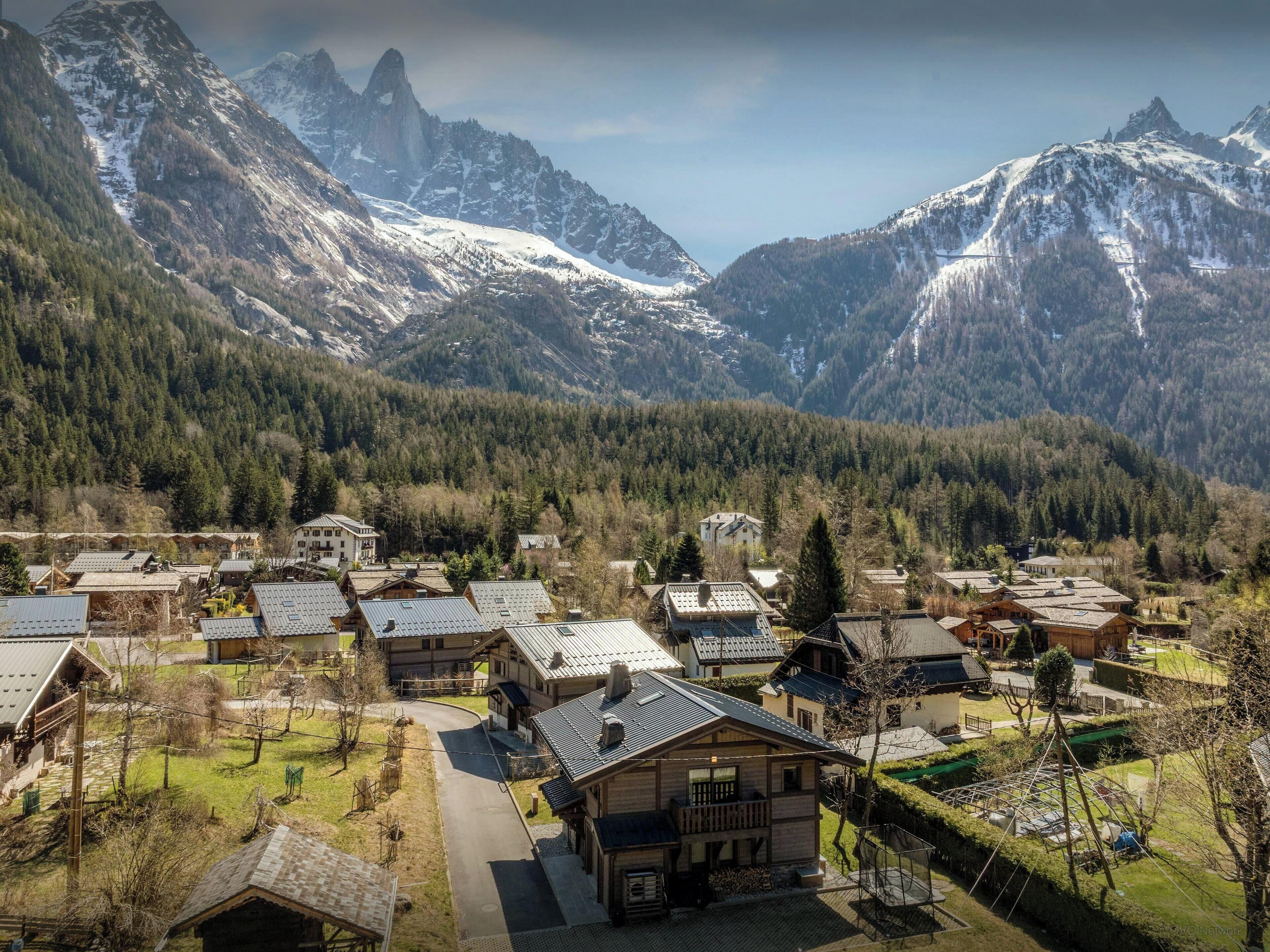 A mountainous village with traditional wooden houses, a central building with a balcony, and a clear view of the surrounding peaks.