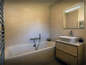 Ein modernes Badezimmer mit einer Badewanne, einem Waschtisch und einem Spiegel.