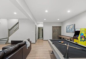 A modern indoor space with a pool table, a sofa, a staircase, and a door leading to another room.