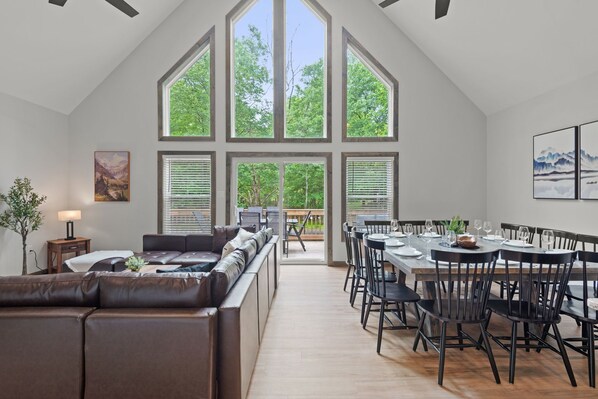 A spacious living area with a large window, a dining table with chairs, and a leather sofa.