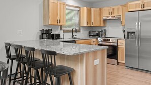 A modern kitchen with wooden cabinets, a granite countertop, a stainless steel refrigerator, and a built-in oven. - The Ultimate Social Stay - 6BRs, Hot Tub, Arcade, Fire Pit. SUMMER SAVINGS! (Albrightsville)