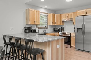A modern kitchen with wooden cabinets, a granite countertop, a stainless steel refrigerator, and a built-in oven.