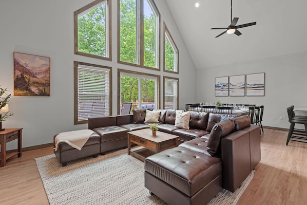 A spacious living room with a sectional sofa, a coffee table, and large windows with blinds.