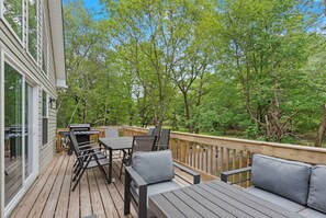 A wooden deck with outdoor furniture, a grill, and a view of a wooded area. - The Ultimate Social Stay - 6BRs, Hot Tub, Arcade, Fire Pit. SUMMER SAVINGS! (Albrightsville)