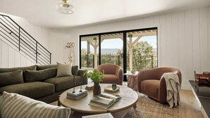 A living room with a sofa, armchair, coffee table, and a view through large windows. - Highland Haus (stunning lakeview + private dock!) (Lake Arrowhead)