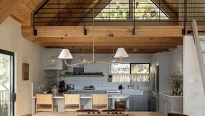 A spacious kitchen with a dining area, wooden ceiling beams, and a view of the outdoors. - Highland Haus (stunning lakeview + private dock!) (Lake Arrowhead)