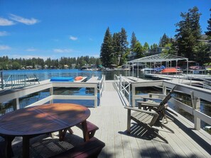 A wooden deck with a table and chairs, a pool, and a dock with boats. - Highland Haus (stunning lakeview + private dock!) (Lake Arrowhead)