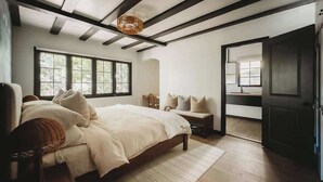 Une chambre à coucher avec un grand lit, un banc et une porte donnant sur une autre pièce.