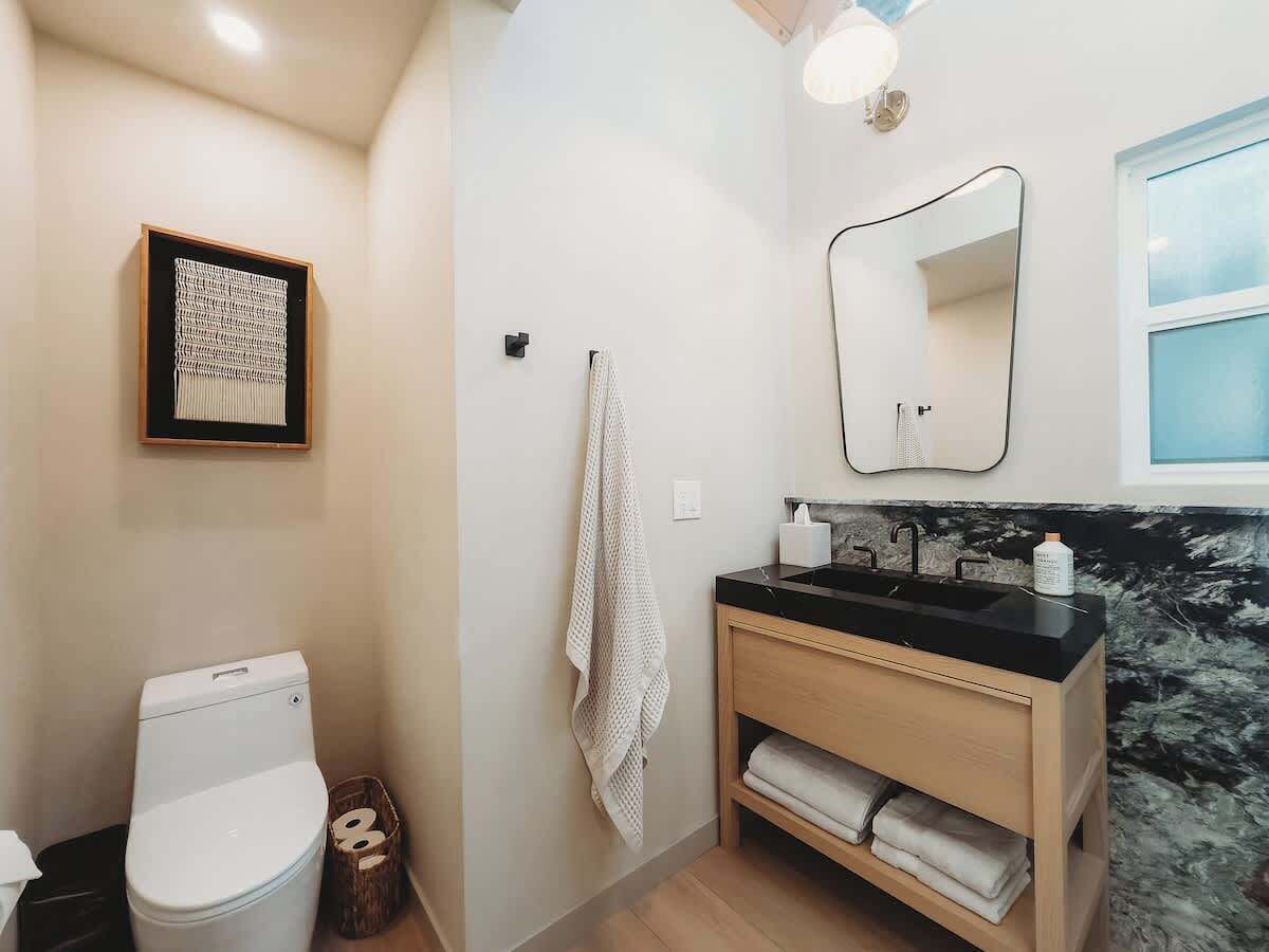 Une salle de bain équipée de toilettes, d’un lavabo, d’un miroir, d’un porte-serviettes et d’une œuvre d’art encadrée accrochée au mur.