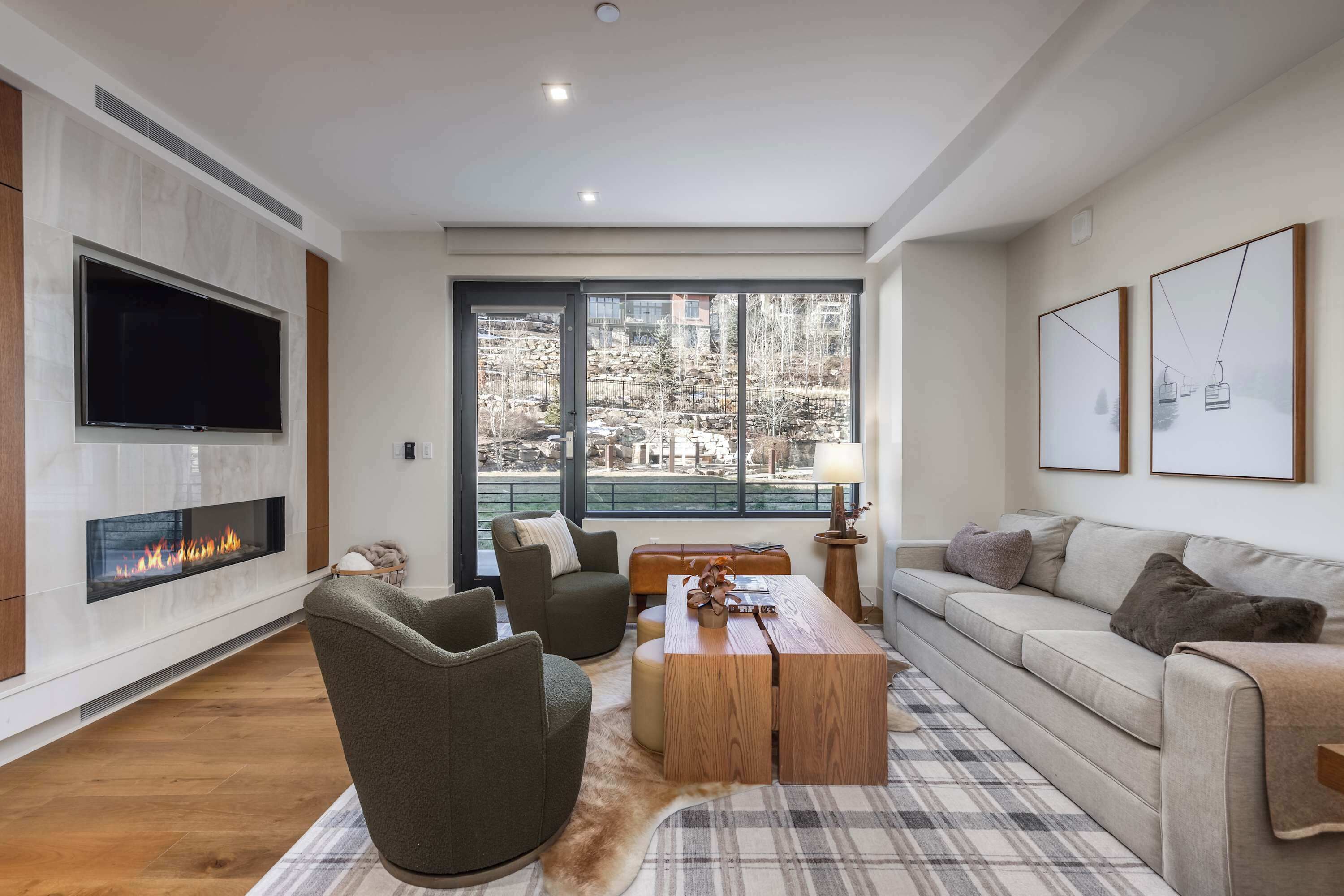 A modern living room with a fireplace, seating, large windows, and artwork.