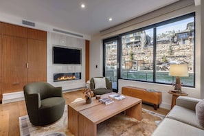 A modern living room with a fireplace, a television, and a large window with a view of a mountainous landscape. - Lift 305 - Ski-In/Ski-Out (Park City)