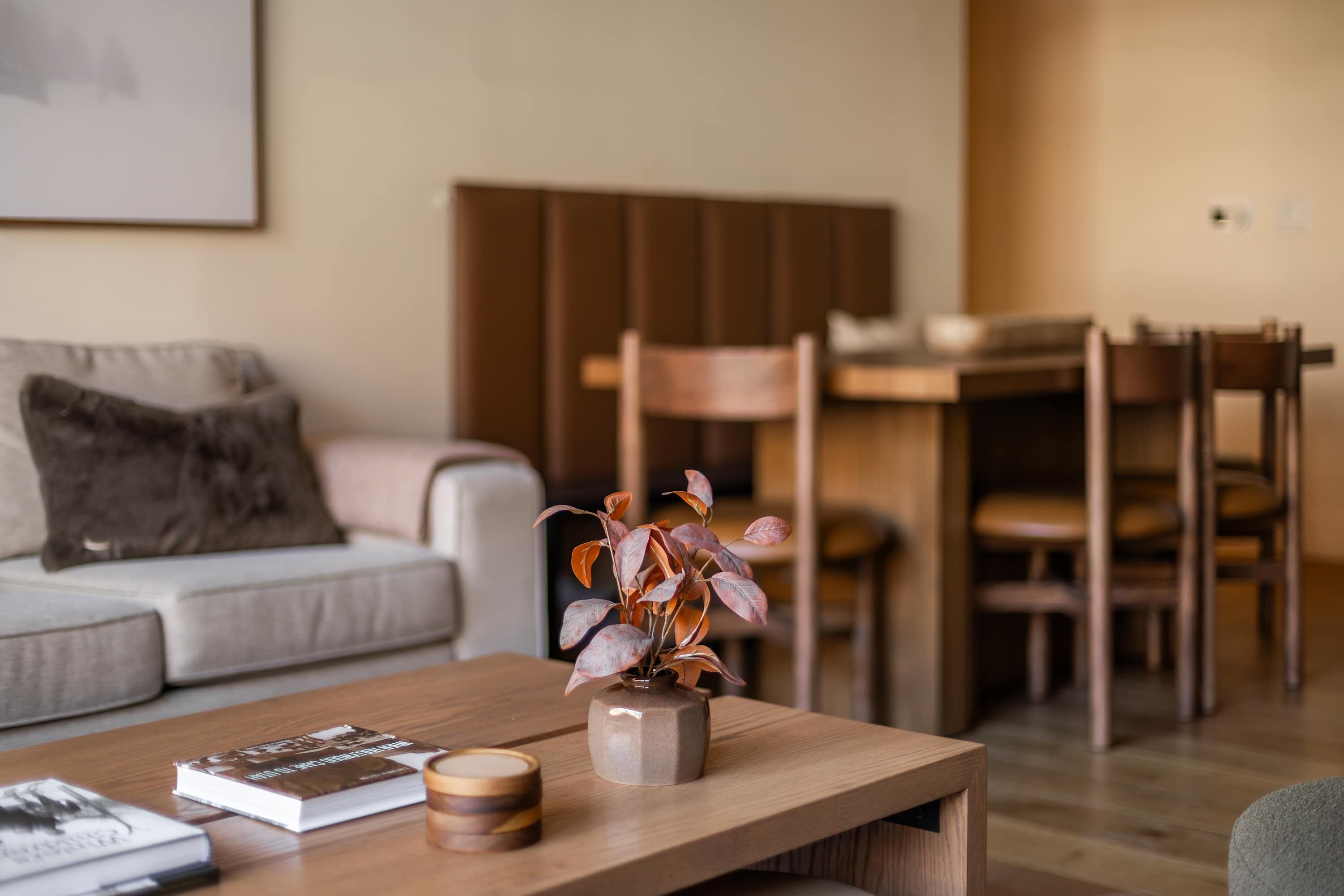 A living room with a sofa, a coffee table with a vase and books, a dining area with chairs and a table.