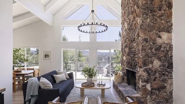 A spacious living area with a stone fireplace, a large window, and a hanging light fixture. - West Shore Waterview, (walk to lake & North Bay!) (Lake Arrowhead)