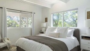 A bedroom with a bed, nightstands, a chair, and large windows. - West Shore Waterview, (walk to lake & North Bay!) (Lake Arrowhead)