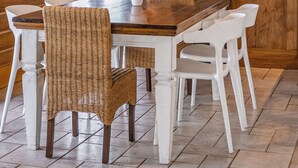 L’intérieur d’un chalet en bois comprend une table à manger, des chaises en osier, un vase blanc orné de fleurs et un coin cuisine avec des meubles blancs.