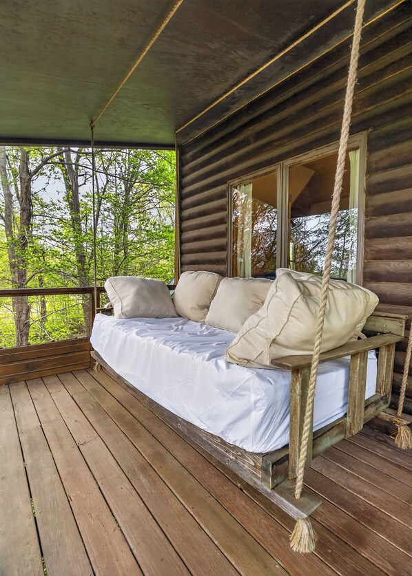 A wooden deck with a swing bed featuring white bedding and beige pillows.