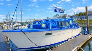 A boat docked at a marina with a clear sky, other boats in the background, and a flag on top. - Sleep in a Van Gogh painting! A floating tribute to the art of Vincent. (League City)