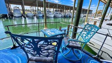 Un port de plaisance avec des bateaux amarrés, un espace de repos couvert avec des chaises et une table, et un ciel dégagé.