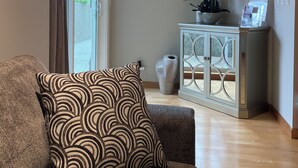 A living room with a sofa, a vase with flowers, a cabinet, and a window with curtains. - Cozy Oceanmount 1BR Suite with Sofa Bed – Ideal Escape (Gibsons)