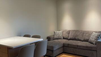 A modern living room with a dining table, grey sofa, and patterned cushions.