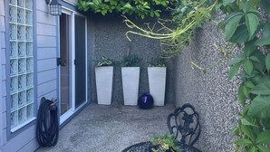 A patio with a table and chairs, a hose, and three potted plants against a wall. - Cozy Oceanmount 1BR Suite with Sofa Bed – Ideal Escape (Gibsons)