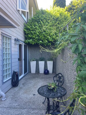 A patio with a table and chairs, a hose, and three potted plants against a wall. - Cozy Oceanmount 1BR Suite with Sofa Bed – Ideal Escape (Gibsons)