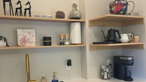 A modern kitchen with a stainless steel sink, wooden cabinets, a coffee maker, and decorative items on shelves. - Cozy Oceanmount 1BR Suite with Sofa Bed – Ideal Escape (Gibsons)
