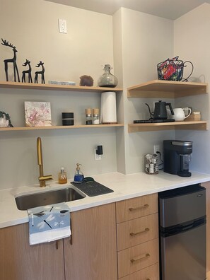 A modern kitchen with a stainless steel sink, wooden cabinets, a coffee maker, and decorative items on shelves.