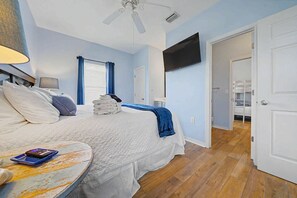 Ein Schlafzimmer mit einem Bett, einem Nachttisch, einem Deckenventilator, einem an der Wand montierten Fernseher und einer Tür zu einem weiteren Raum.