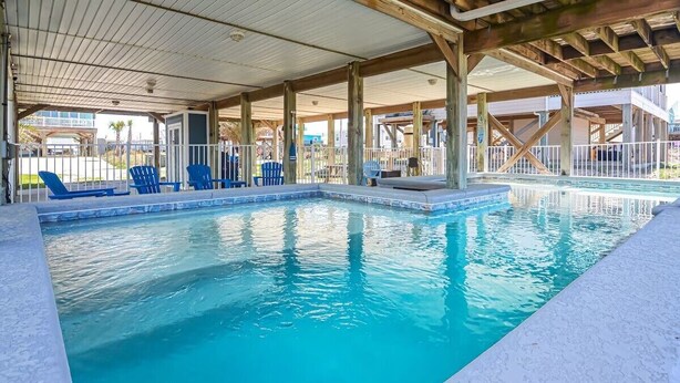 A covered swimming pool with blue chairs and a wooden deck structure. - New listing! Private pool, steps to the beach (Gulf Shores)