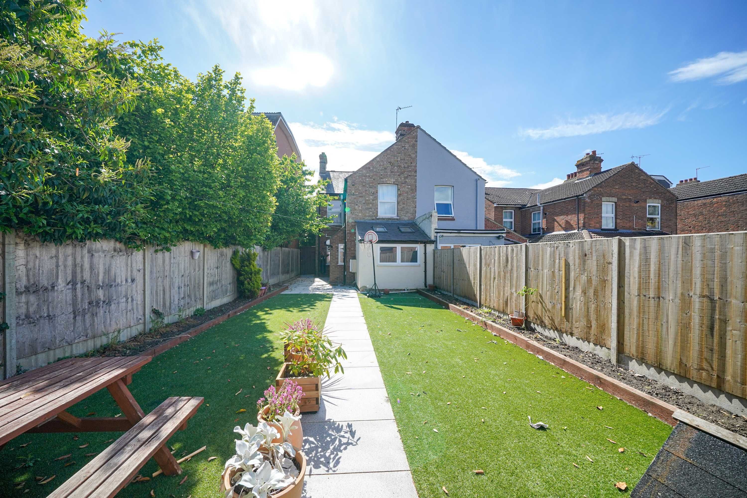 A residential backyard with a wooden fence, a paved pathway, and a small garden area with potted plants.
