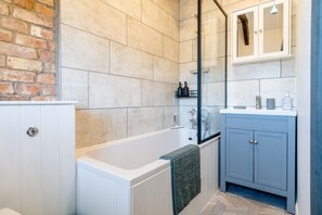 A bathroom with a bathtub, a glass-enclosed shower, a white cabinet, and a blue cabinet.