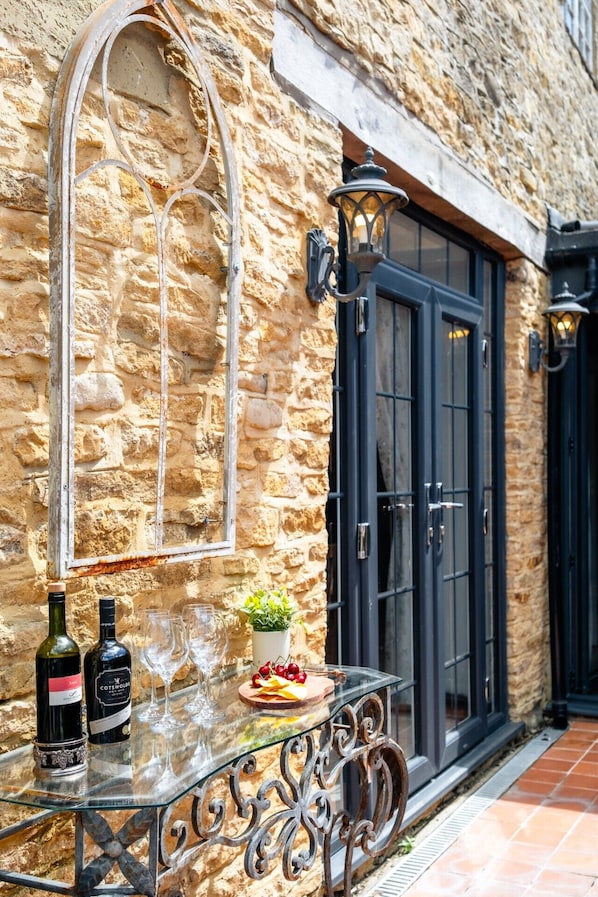 A stone building with a glass table, two wine bottles, and a plate of grapes.