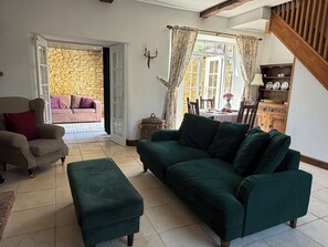 A living room with a green sofa, a beige armchair, and a wooden cabinet with dishes.