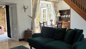 Un salon avec un canapé vert, un pouf assorti, un coin repas comprenant une table et des chaises, et un escalier.
