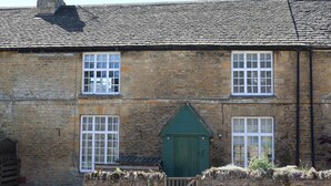 Un bâtiment en pierre avec une porte verte, de nombreuses fenêtres et une cheminée en briques.