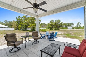 A covered patio with outdoor furniture, a ceiling fan, and a view of the surrounding landscape.