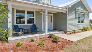 A single-story house with a porch, two blue Adirondack chairs, and a small garden area. - Fall Deals + Snowbird Rates | Coastal Stay With Bay Views (Eastpoint)