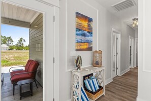 A hallway with a view to the outside, a red chair, a painting, and a console table with towels.