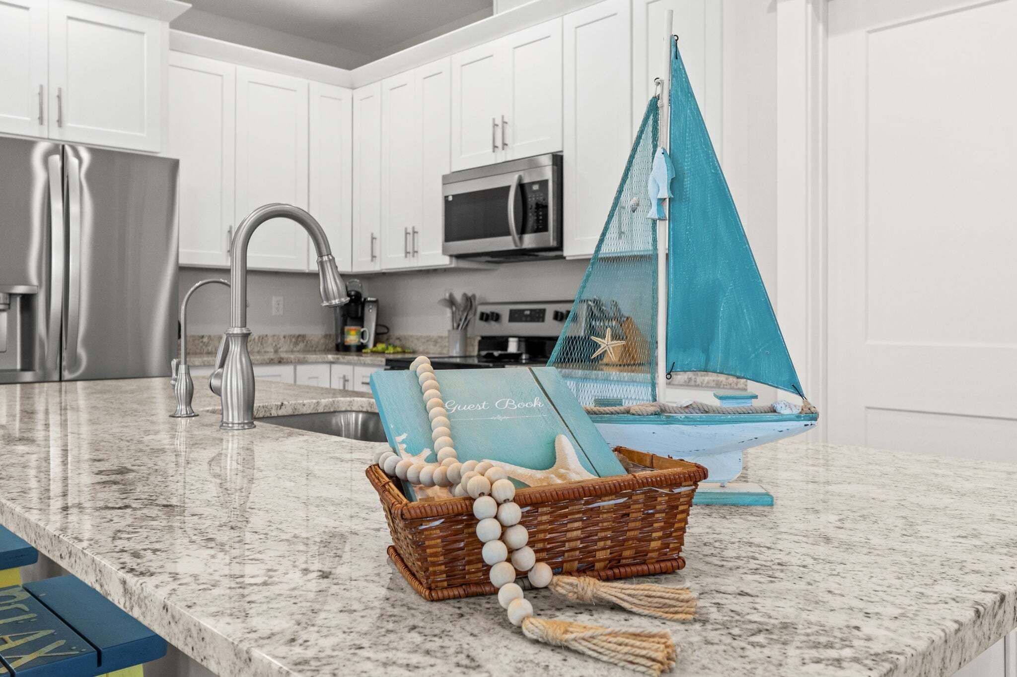 A kitchen with white cabinets, stainless steel appliances, and a blue decorative sailboat on the counter.