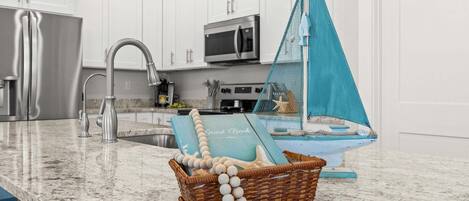 A kitchen with white cabinets, stainless steel appliances, and a blue decorative sailboat on the counter.